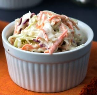 A ramekin of creamy coleslaw with shredded cabbage and carrot.