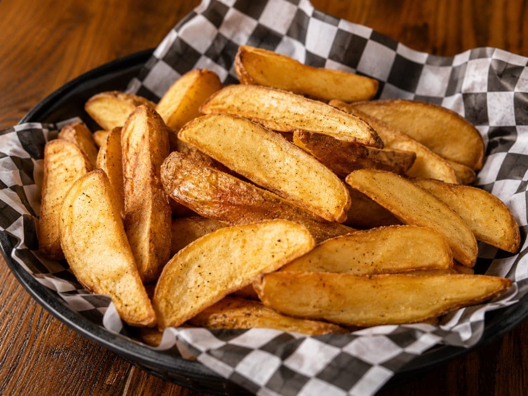 A basket of fries topped with grilled steak, green onion, tomato and onion.