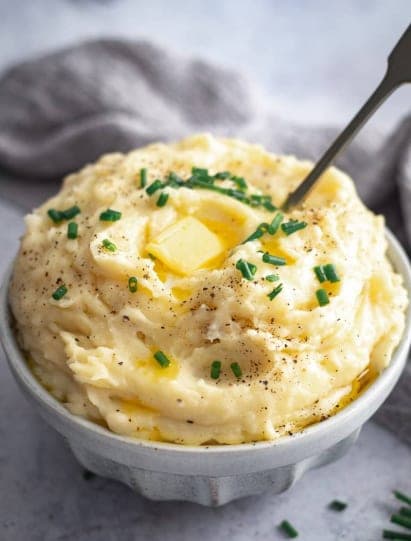 A bowl of mashed potatoes with melting butter and chopped chives.