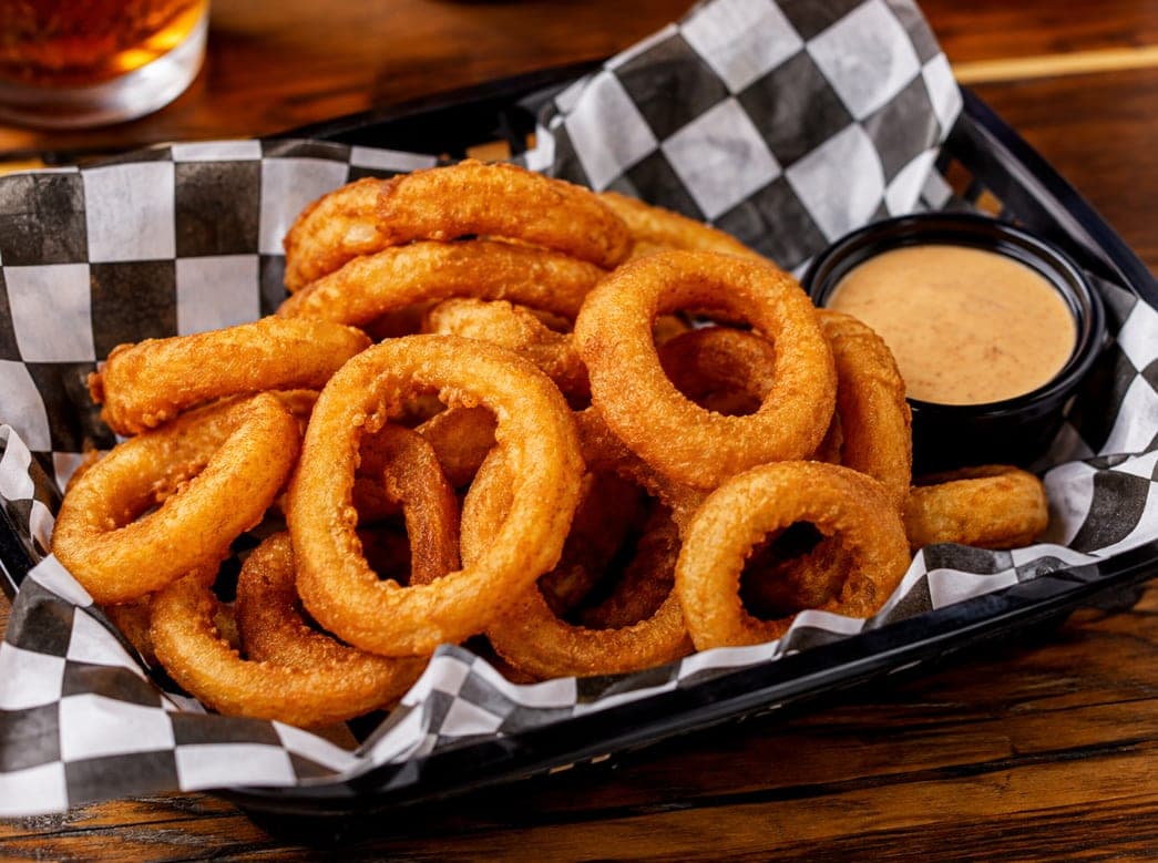 A basket of battered onion rings with a side of dipping sauce.