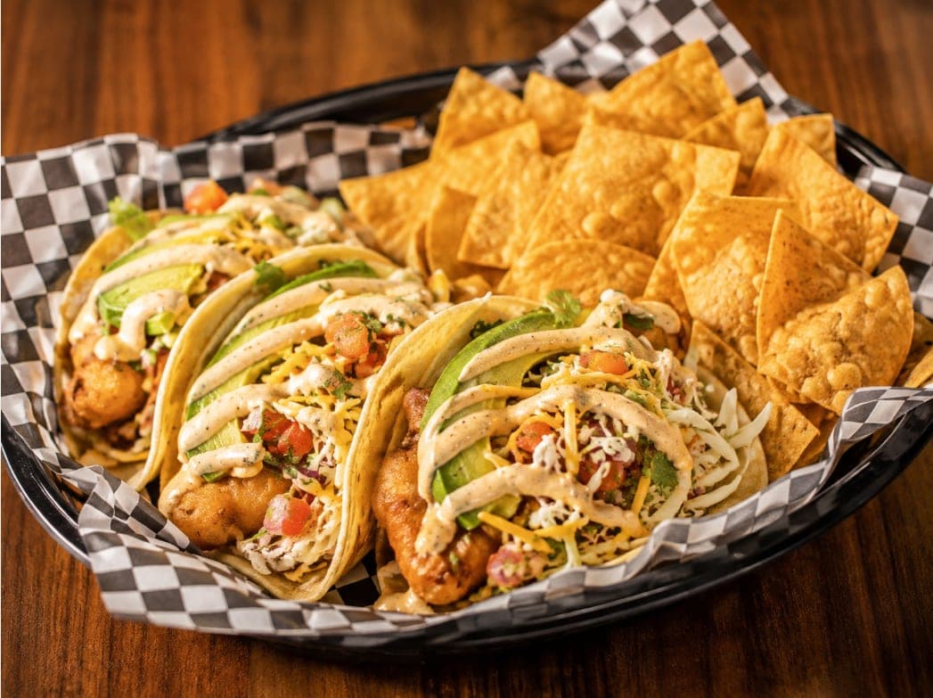 Three fish tacos with avocado, pico de gallo, cheese and chipotle crema, with tortilla chips.