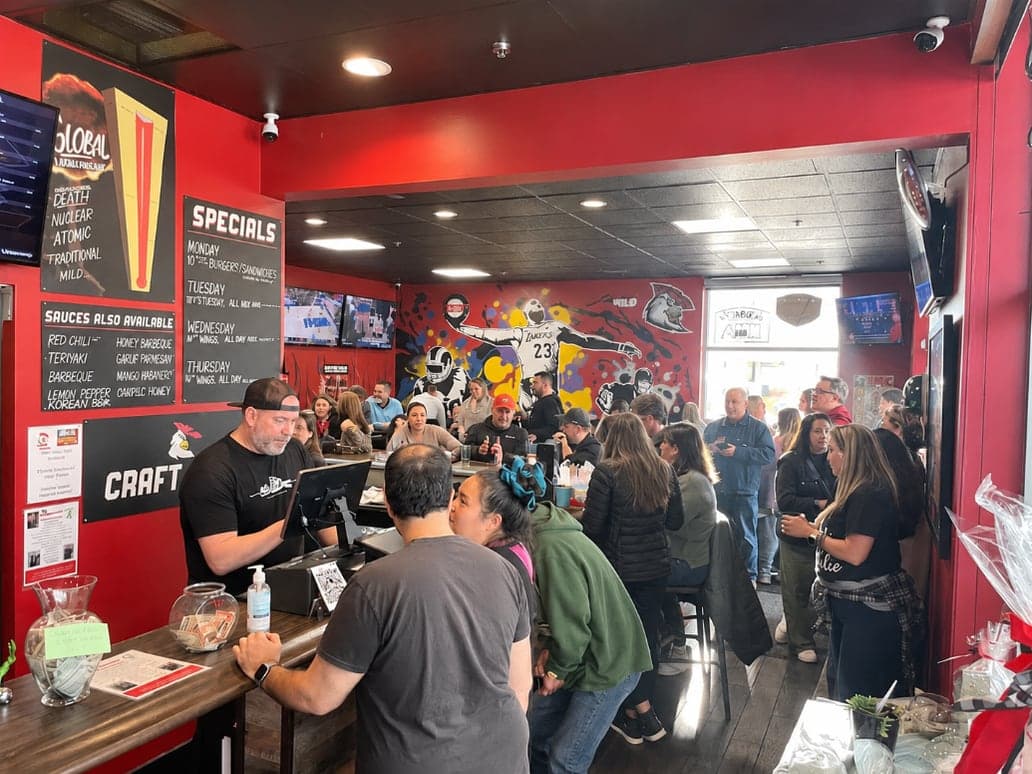 A packed Wicked Chicken dining room, with guests at the counter and along the bar under the sauce board.